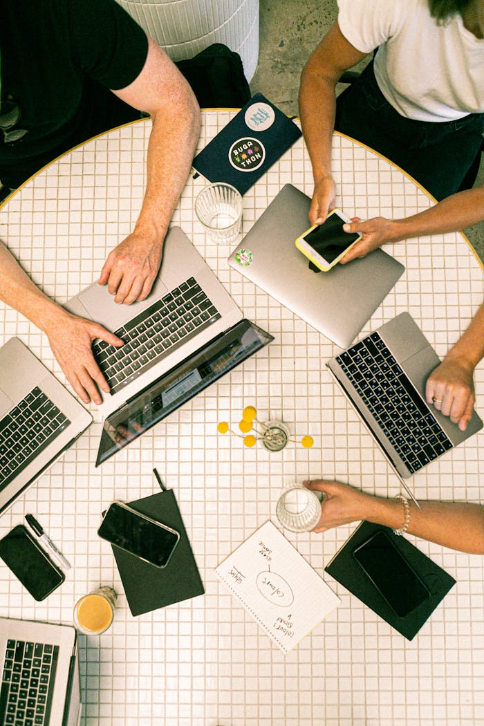 who-we-are Top view of a team collaborating with laptops, phones, and notes in a modern office.
